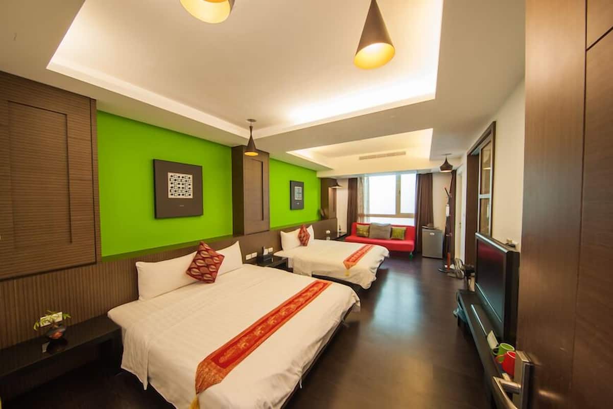 A hotel room with two beds, a sofa, a TV, and a large window.