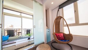 A modern room with a large window, a hanging chair with a red cushion, a blue basin, and a small round ottoman. - HI One One (Magong)