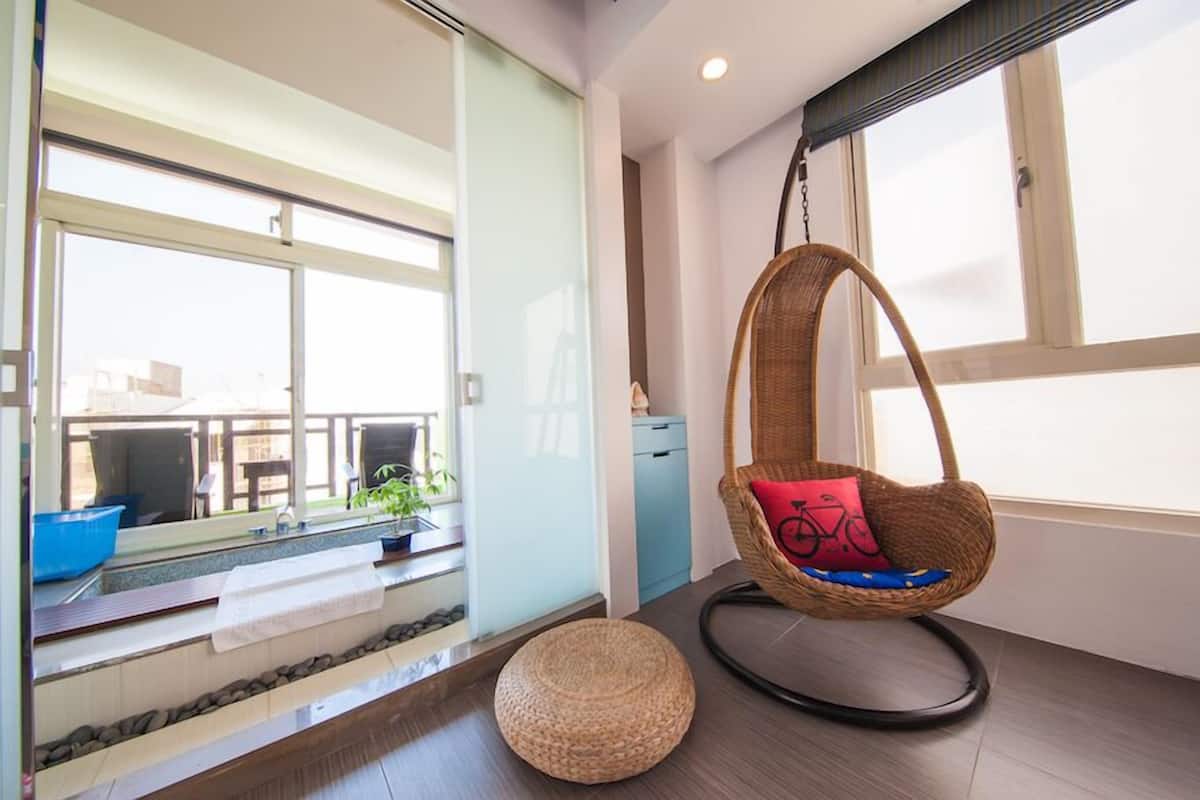 A modern room with a large window, a hanging chair with a red cushion, a blue basin, and a small round ottoman.