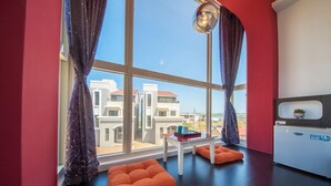 A modern room with large windows, orange cushions, a small table, and a white cabinet. - HI One One (Magong)