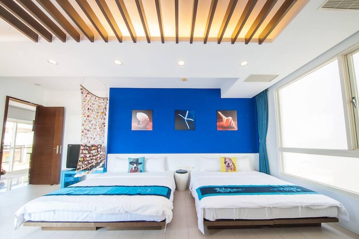 A modern hotel room with two beds, a blue accent wall, and artwork.