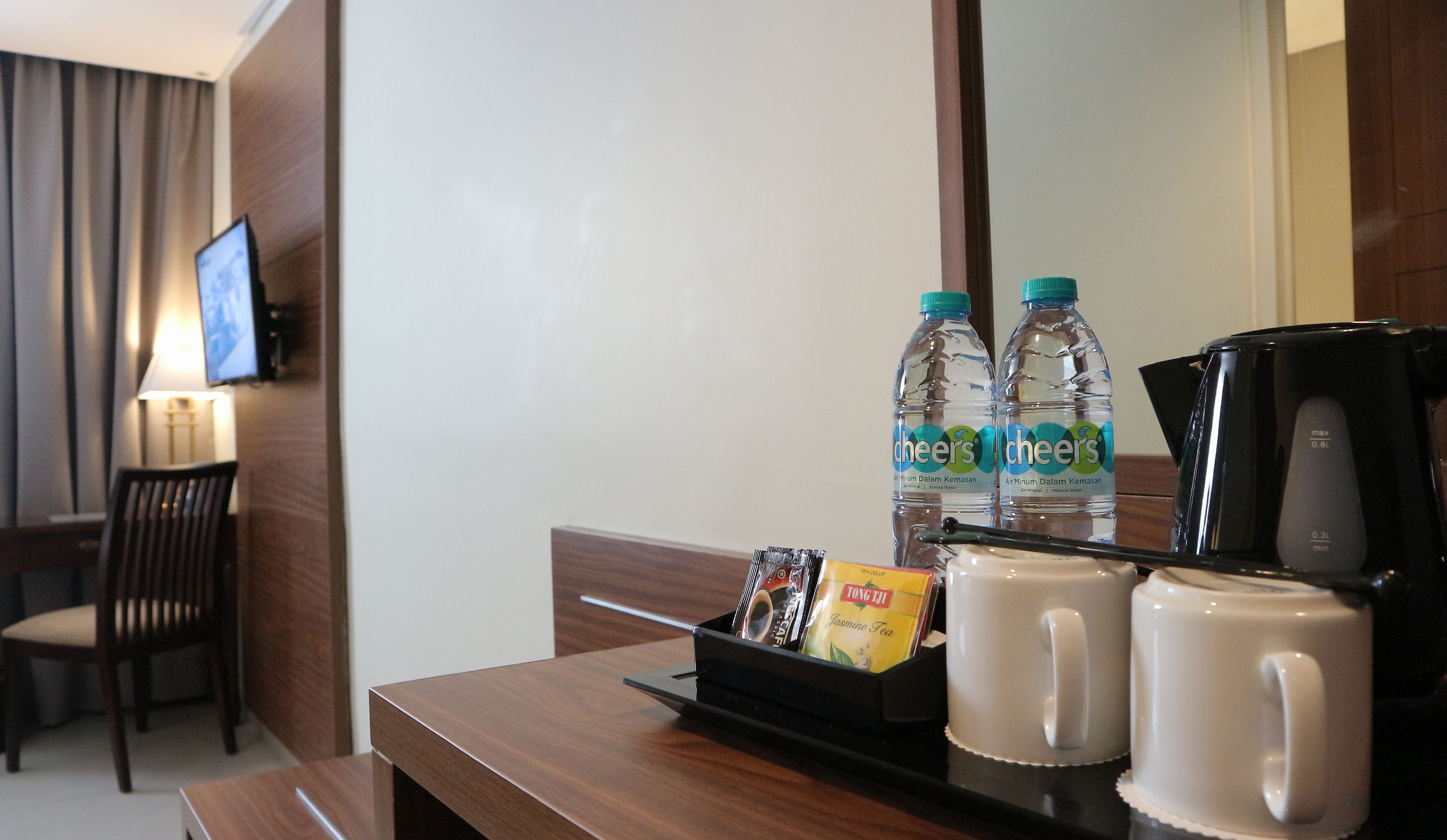 A hotel room with a wooden desk, two water bottles, a coffee maker, and a tray with a tea packet and a cup.