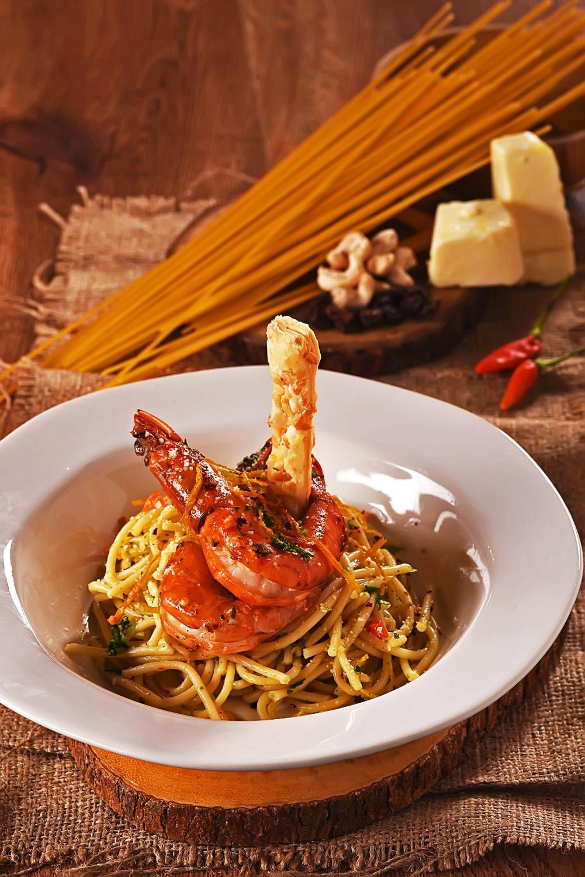 A plate of spaghetti with shrimp and a piece of grilled meat, possibly chicken, garnished with herbs.