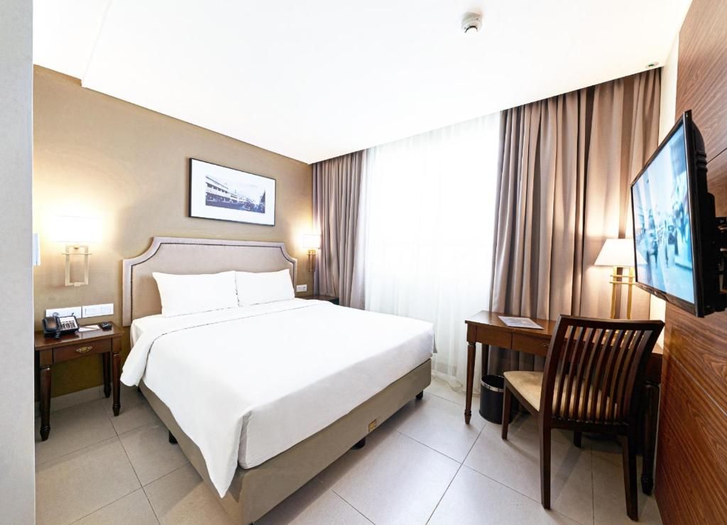 Una camera d'albergo con un letto, comodino, lampada, scrivania, sedia, televisore e tende.