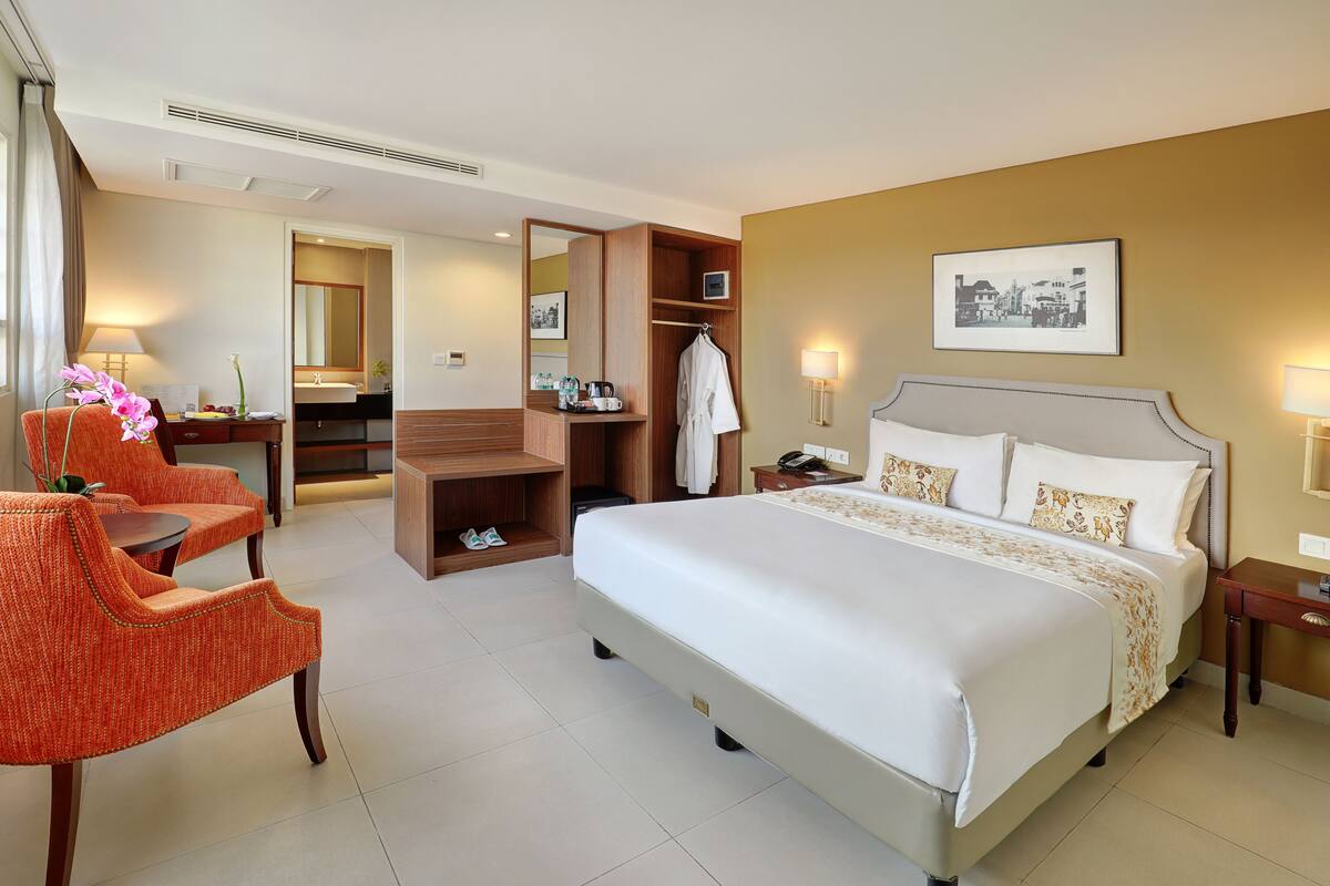 Ein Hotelzimmer mit einem großen Bett, einem Schreibtisch mit Stuhl, einem Kleiderschrank und einem durch eine offene Tür einsehbarer Badezimmer.