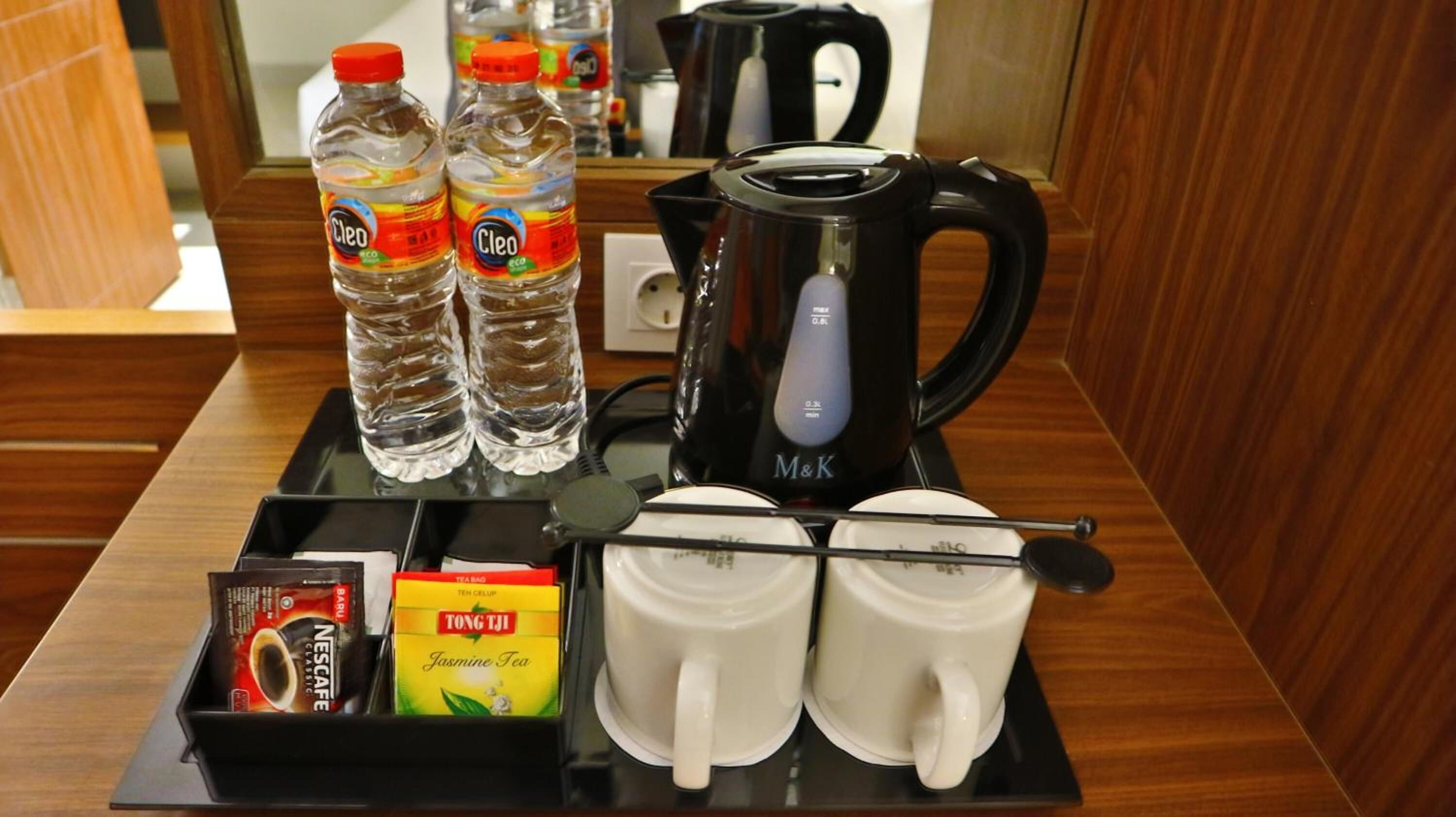 En hotellrumsvagn med frukosttillbehör: vatten på flaska, en kaffebryggare, tepåsar och tekoppar.