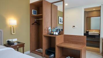 A hotel room with a wooden wardrobe, a desk with a telephone, a bedside lamp, and a mirror.