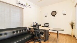 A modern office space with a black leather sofa, a desk with a chair, a small round table, and wall clocks labeled with country names. - Itsy Hotels Riyas Grand (Tirupati)