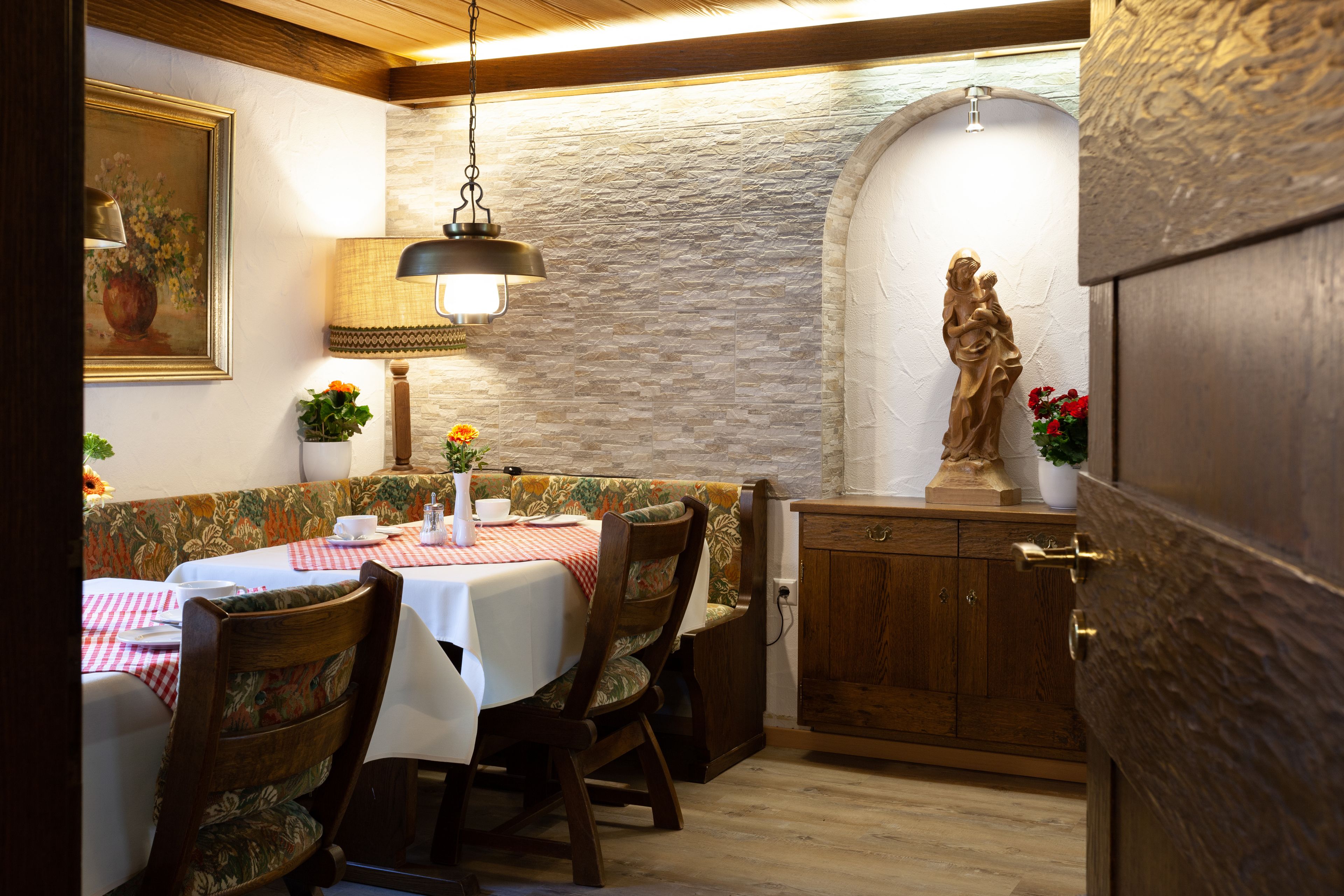 Un comedor con pared de piedra, mobiliario de madera y una estatua.