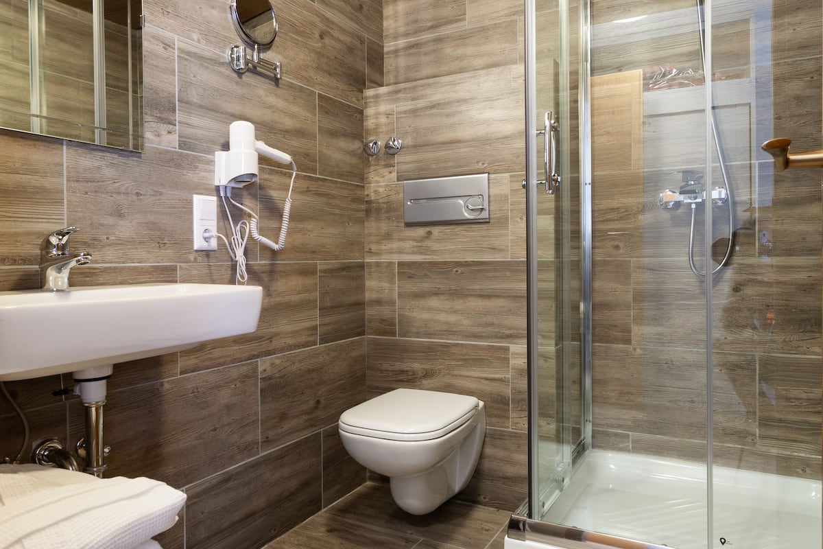 A modern bathroom with a wooden floor, a glass shower enclosure, a white sink, and a toilet.