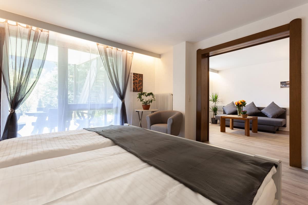 A hotel room with a bed, a chair, a sofa, and a table with plants.