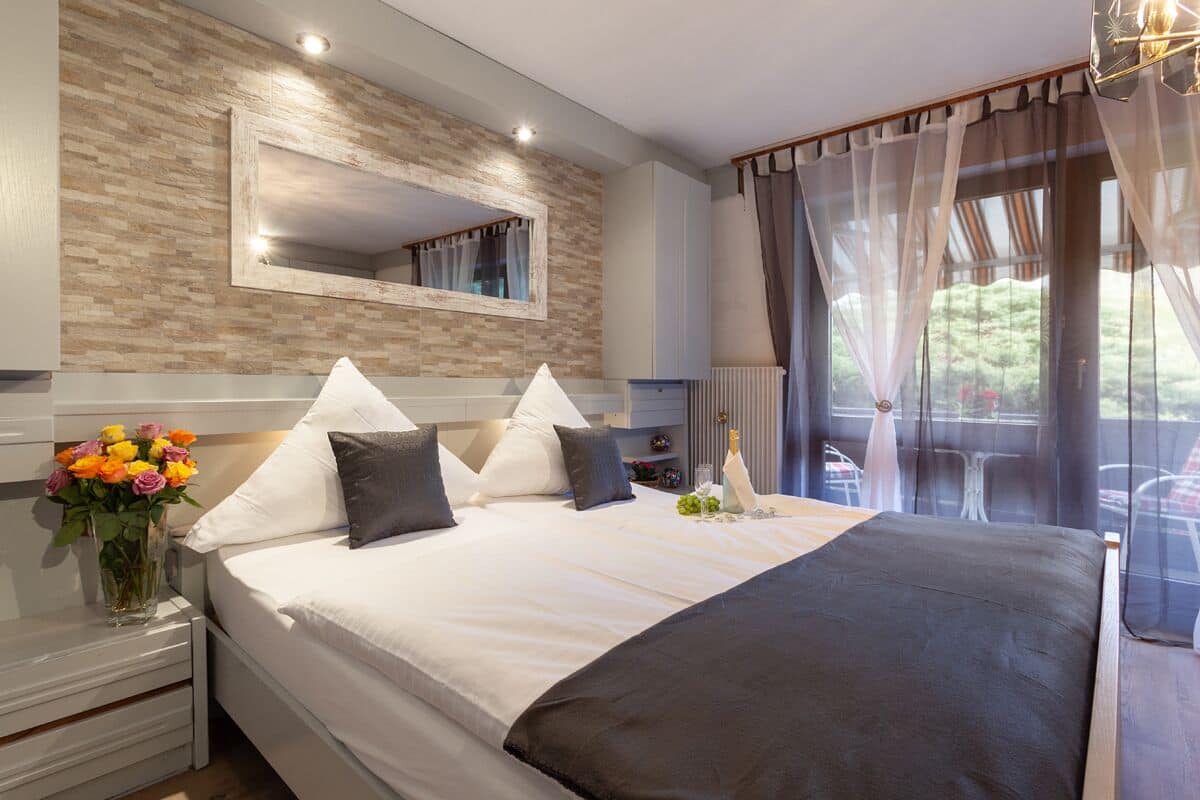 A modern bedroom with a large bed, a mirror, and a view of the outdoors.