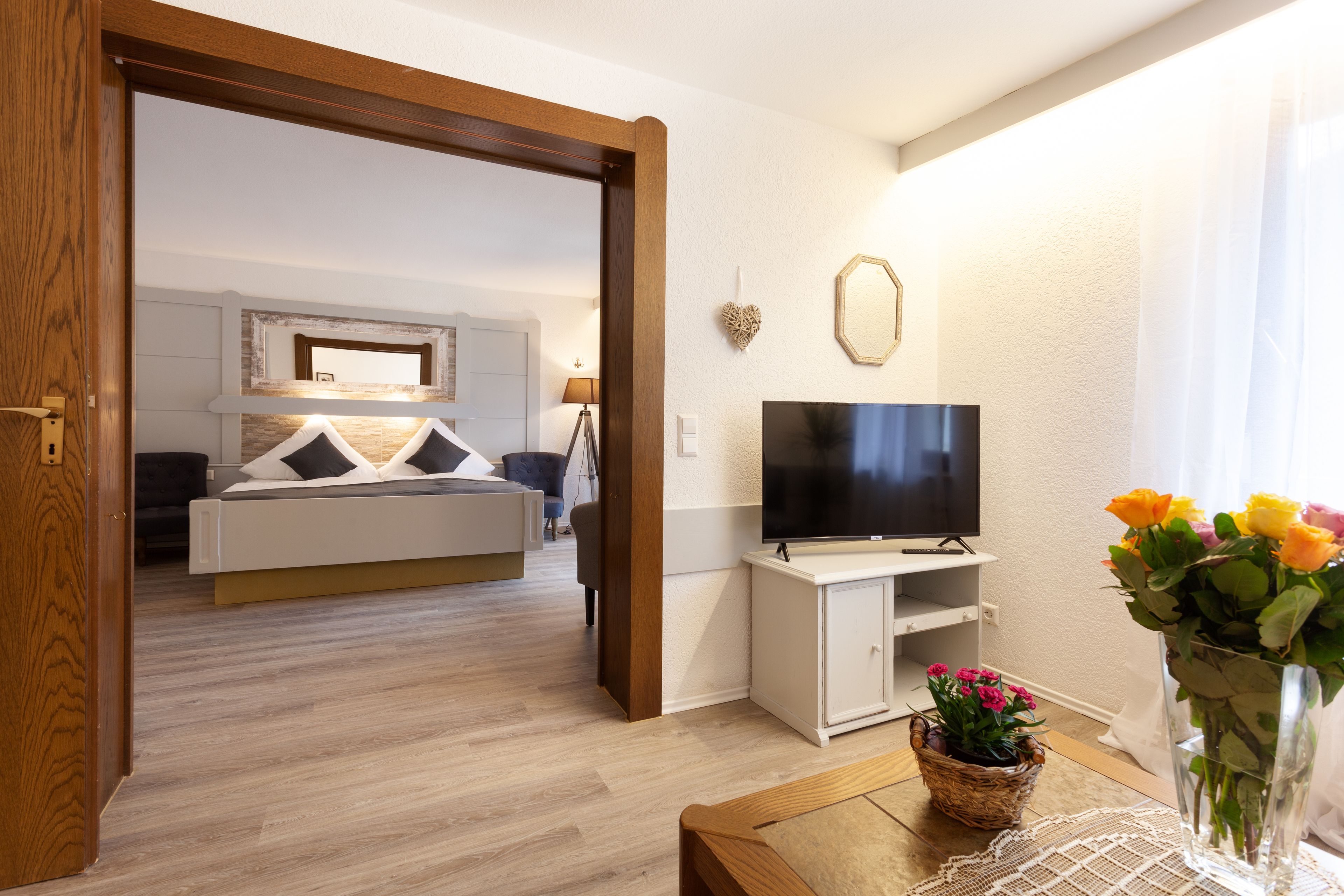 A modern hotel room with a bed, TV, and a vase of flowers.