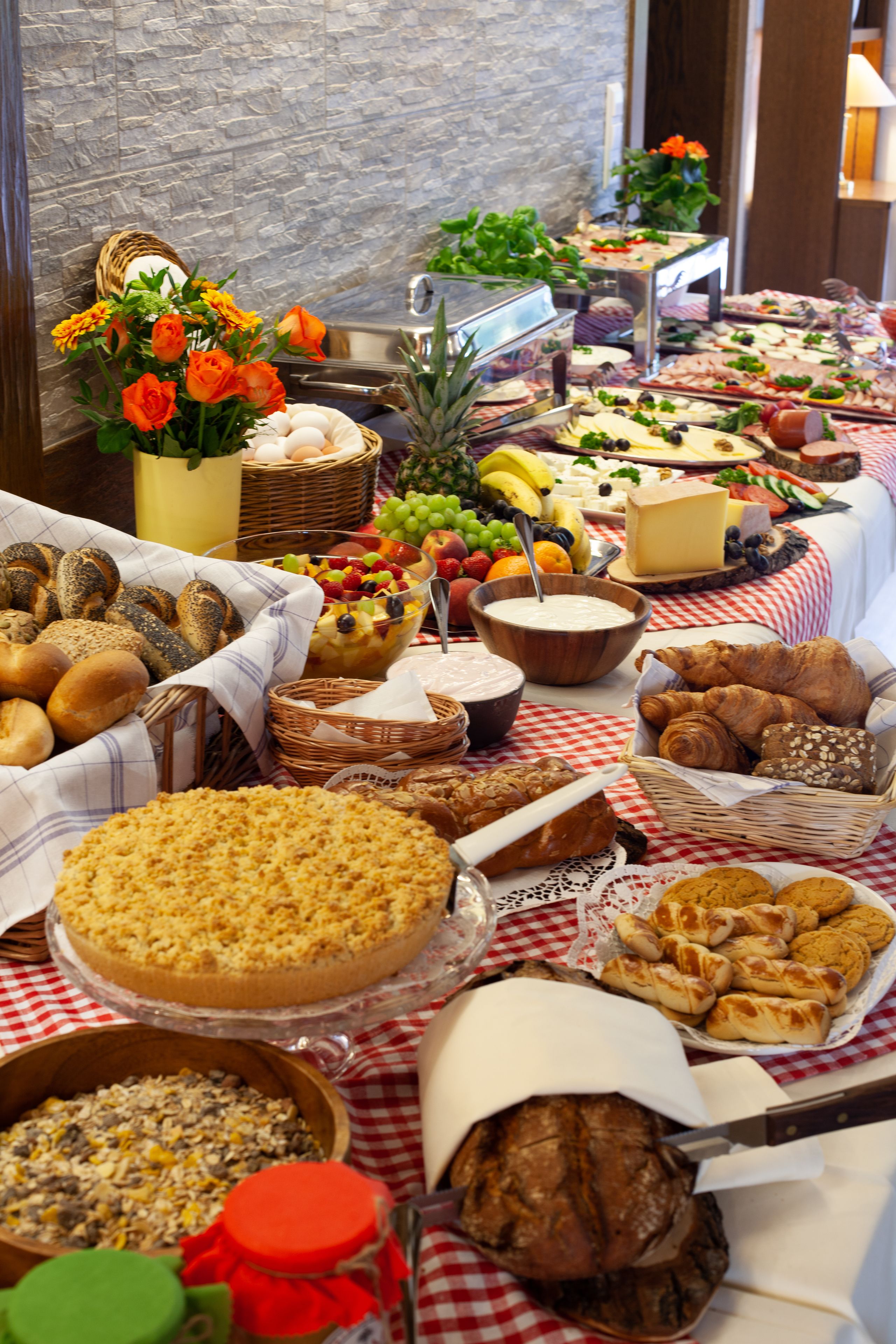 Una mesa de buffet con diferentes alimentos y un jarrón decorativo con flores naranjas.