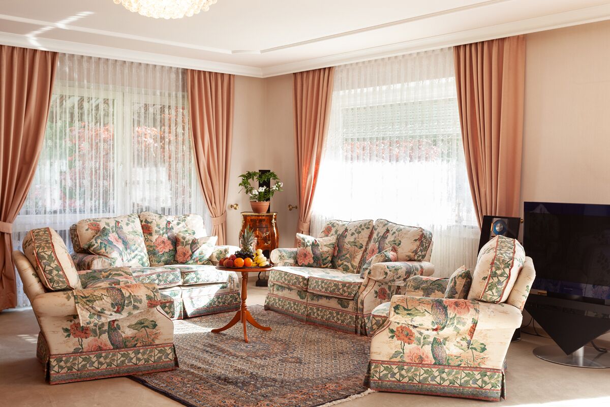A living room with floral-patterned sofas, a coffee table with fruit, and a television.