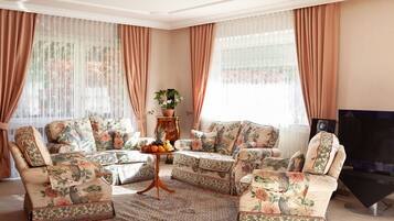 A living room with floral-patterned sofas, a coffee table with fruit, and a television.