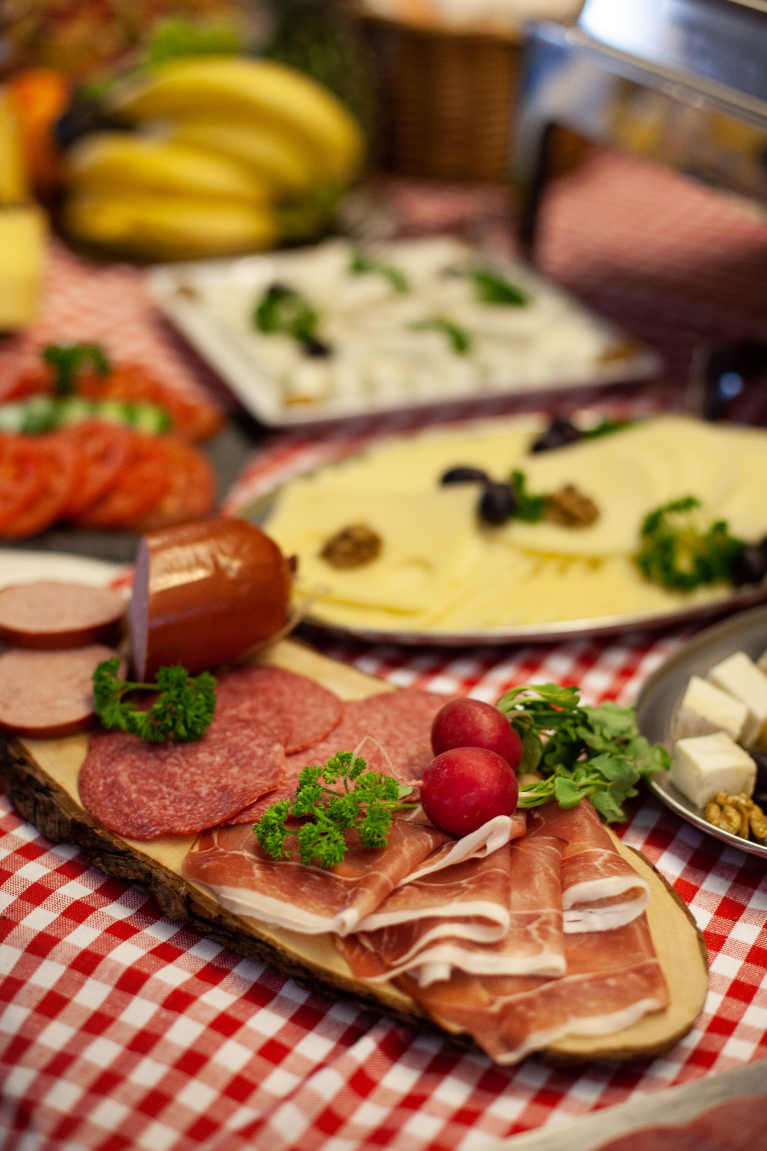 A charcuterie board with various meats, cheeses, and fruits on a checkered tablecloth.