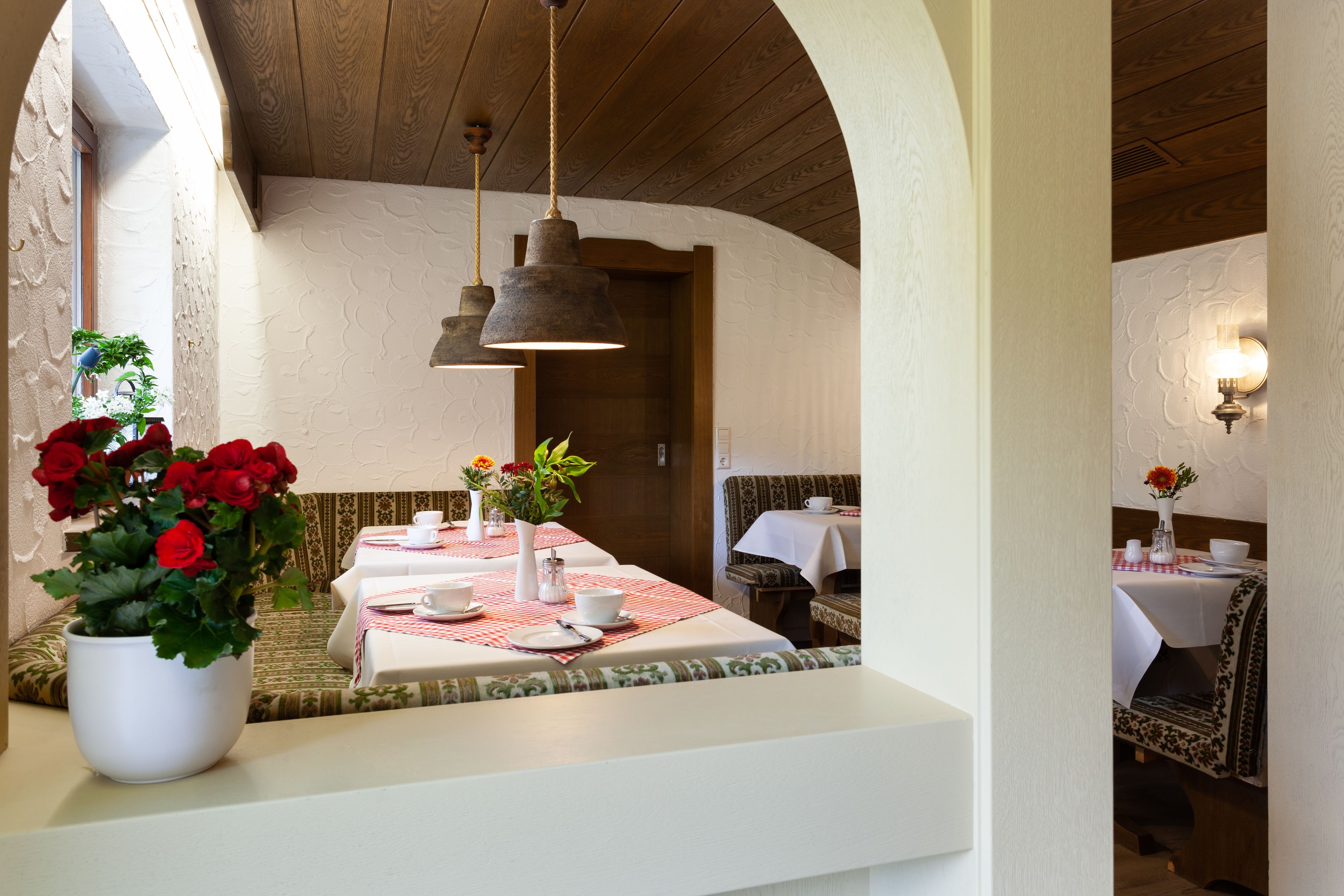 A dining area with a table set for two, a potted plant with red flowers, and a bench.