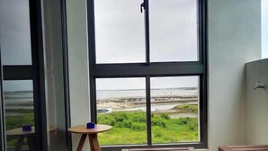 Una habitación con un ventanal amplio que ofrece vistas a un paisaje costero, una mesita redonda y dos bancos de madera.
