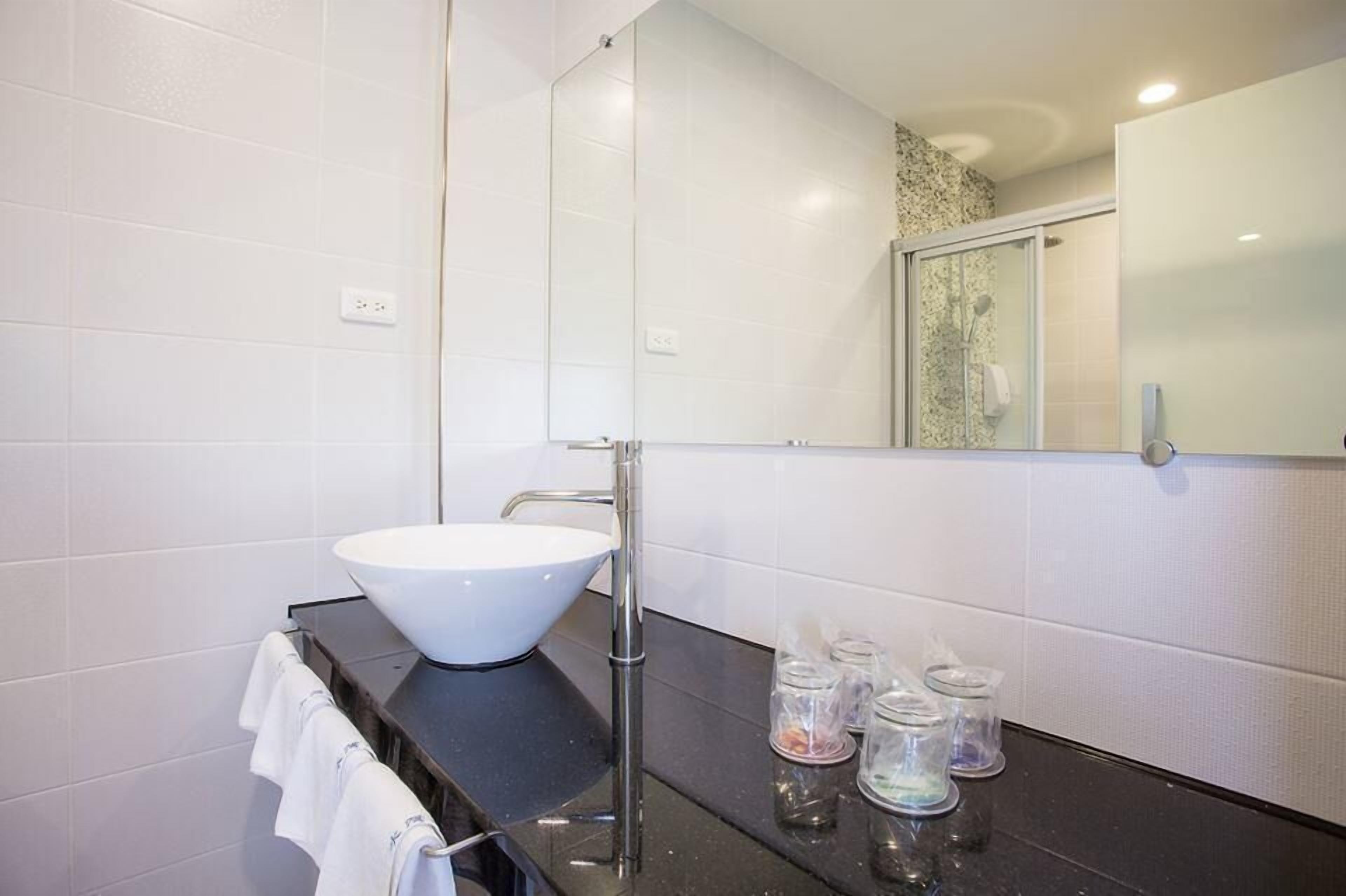 A modern bathroom with a white vessel sink, a large mirror, and a black countertop.