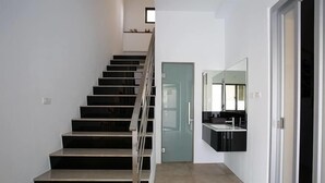 Un interior moderno con una escalera que conduce a un segundo piso, una puerta y una zona de cocina con mostrador y fregadero.