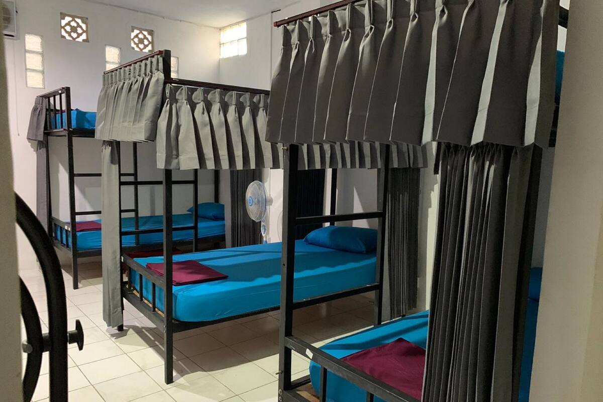 A dormitory room with bunk beds, a fan, and a window with decorative shutters.