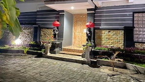 A modern building with a stone facade, a wooden door, and a small garden area with potted plants and a statue. - Arta Garden Guest House & Hostel (Ubud)
