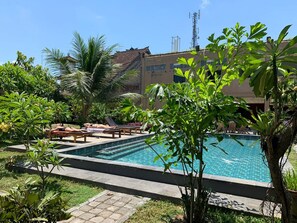 A swimming pool surrounded by lounge chairs and tropical plants, with a building in the background. - Arta Garden Guest House & Hostel (Ubud)