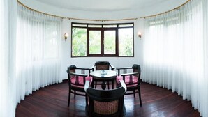 Un coin repas avec une table ronde et quatre chaises, entouré de rideaux blancs et d’une grande fenêtre donnant sur un paysage verdoyant.