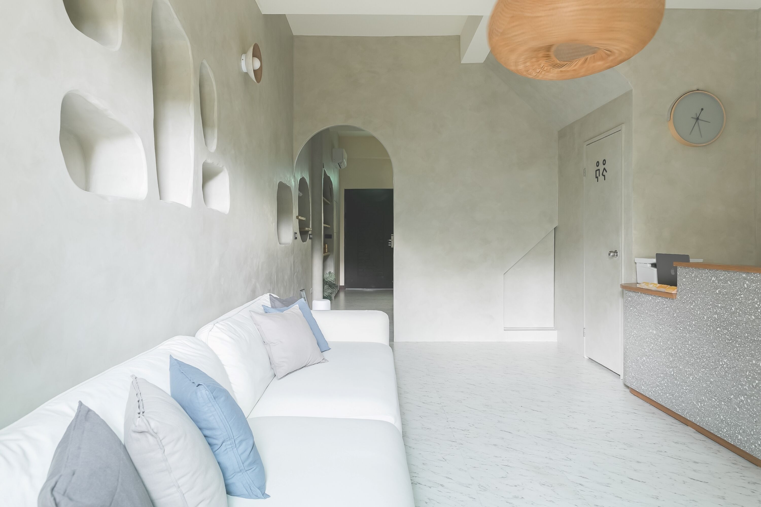 A modern interior with a white sofa, a reception desk, and a hallway leading to another room.