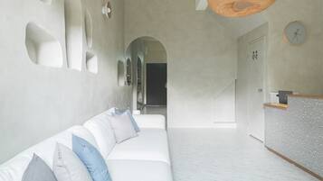 A modern interior with a white sofa, a reception desk, and a hallway leading to another room.