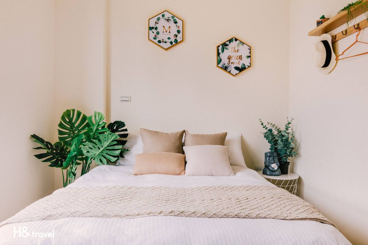 Une chambre à coucher bien rangée, avec un lit, deux décorations murales hexagonales, une plante sur la table de chevet et un chapeau posé sur un porte-chapeau.