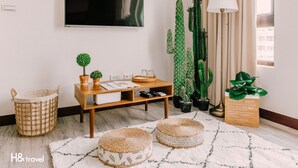 Een moderne woonkamer met een flatscreen televisie, een houten salontafel, rieten manden en een potplant.