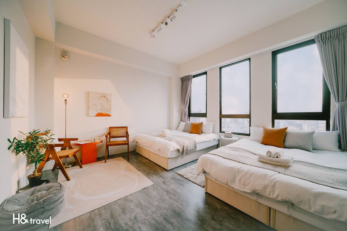 Une chambre d’hôtel moderne avec deux lits, un bureau, une chaise, une plante en pot et de grandes fenêtres.