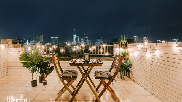 Een terras met een tafel en stoelen, plantenpotten en een uitzicht op de stad bij nacht.