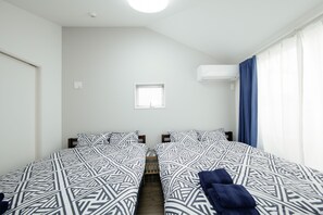 A room with two beds, a small window, an air conditioning unit, and a curtain. - Higashi-Rokugo House WHITE by Tranova (Tokyo)