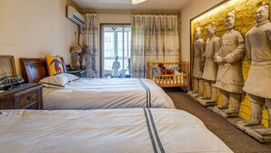 Hotellihuone, jossa on kaksi sänkyä, puinen yöpöytä, lamppu ja suuri seinämaalaus, jossa on kuvattuna muinaisia sotureita.
