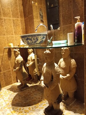 A bathroom with stone tiles, a glass shelf holding a bowl, and a statue of a figure. - Xi'An Warriors Apartment (Xi'an)