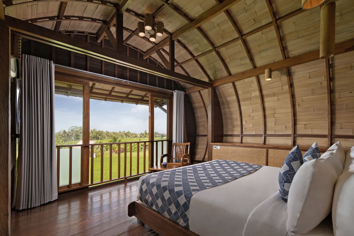 A bedroom with a large bed, wooden ceiling, and a view of a green landscape.
