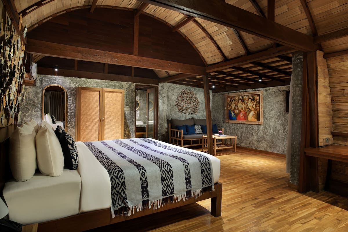 A spacious room with a large bed, wooden beams, a stone wall, a painting, and a cozy seating area.
