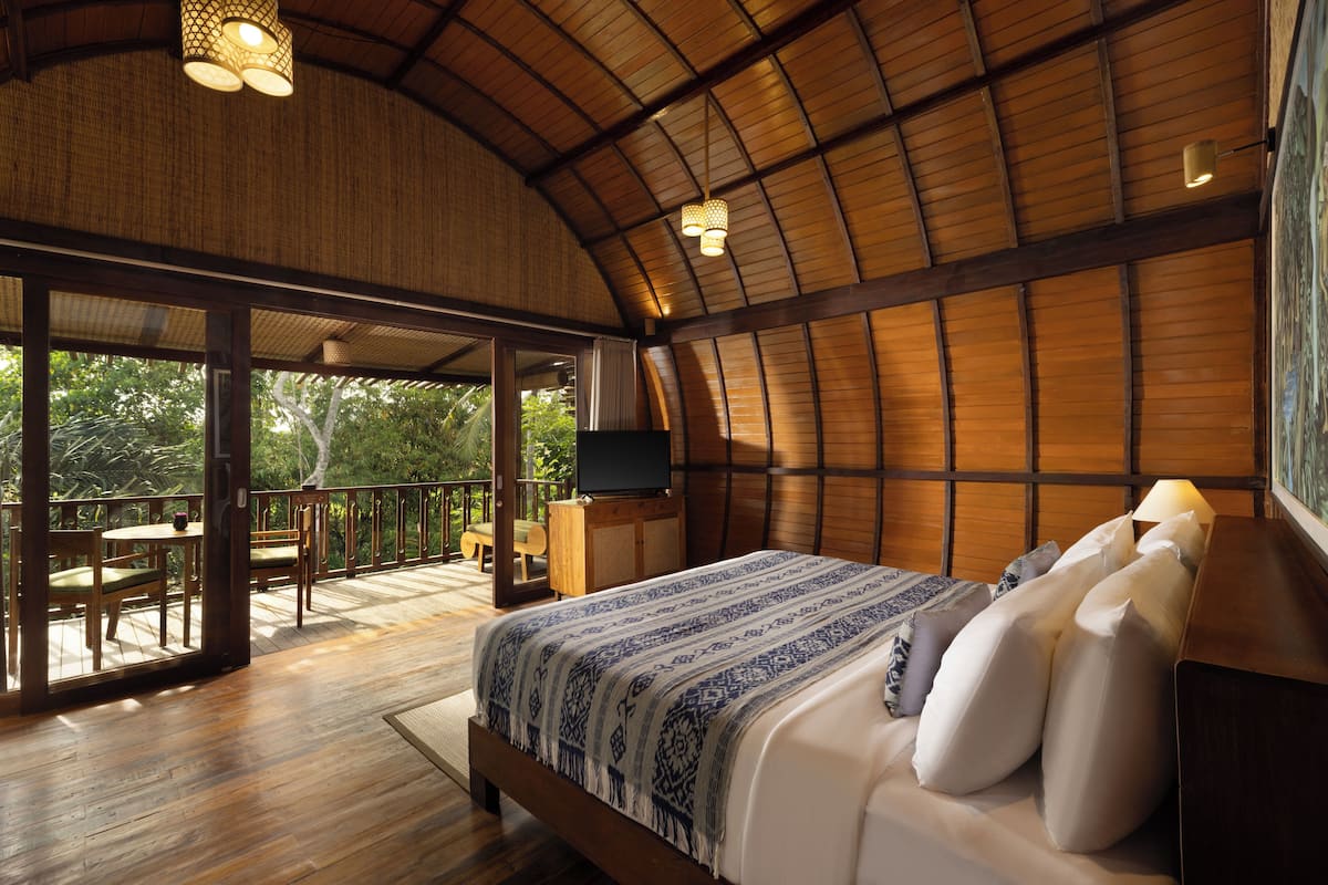 A spacious bedroom with a large bed, a television, and a balcony with wooden furniture.