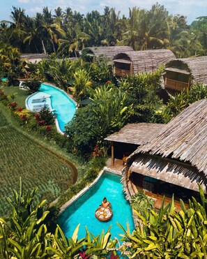Ein Resort mit mehreren Hütten mit Reetdach, einem zentralen Swimmingpool und üppiger tropischer Vegetation.
