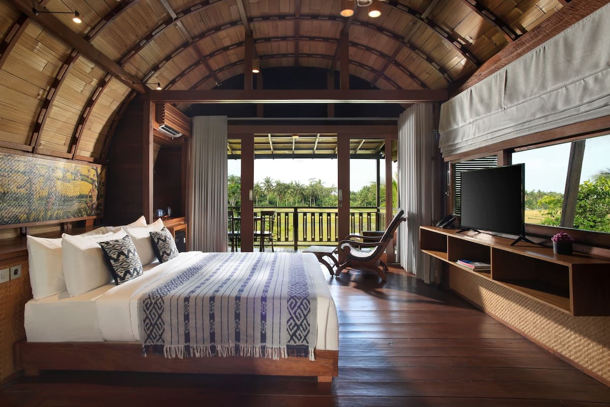 A spacious bedroom with a large bed, a TV, and a balcony with a view of the outdoors.