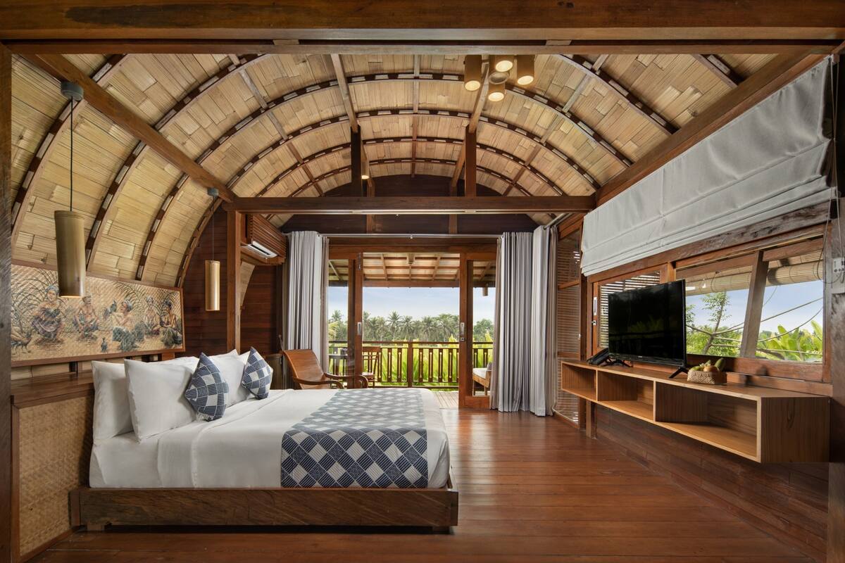 A bedroom with a large bed, wooden ceiling, and a TV on a wooden stand.