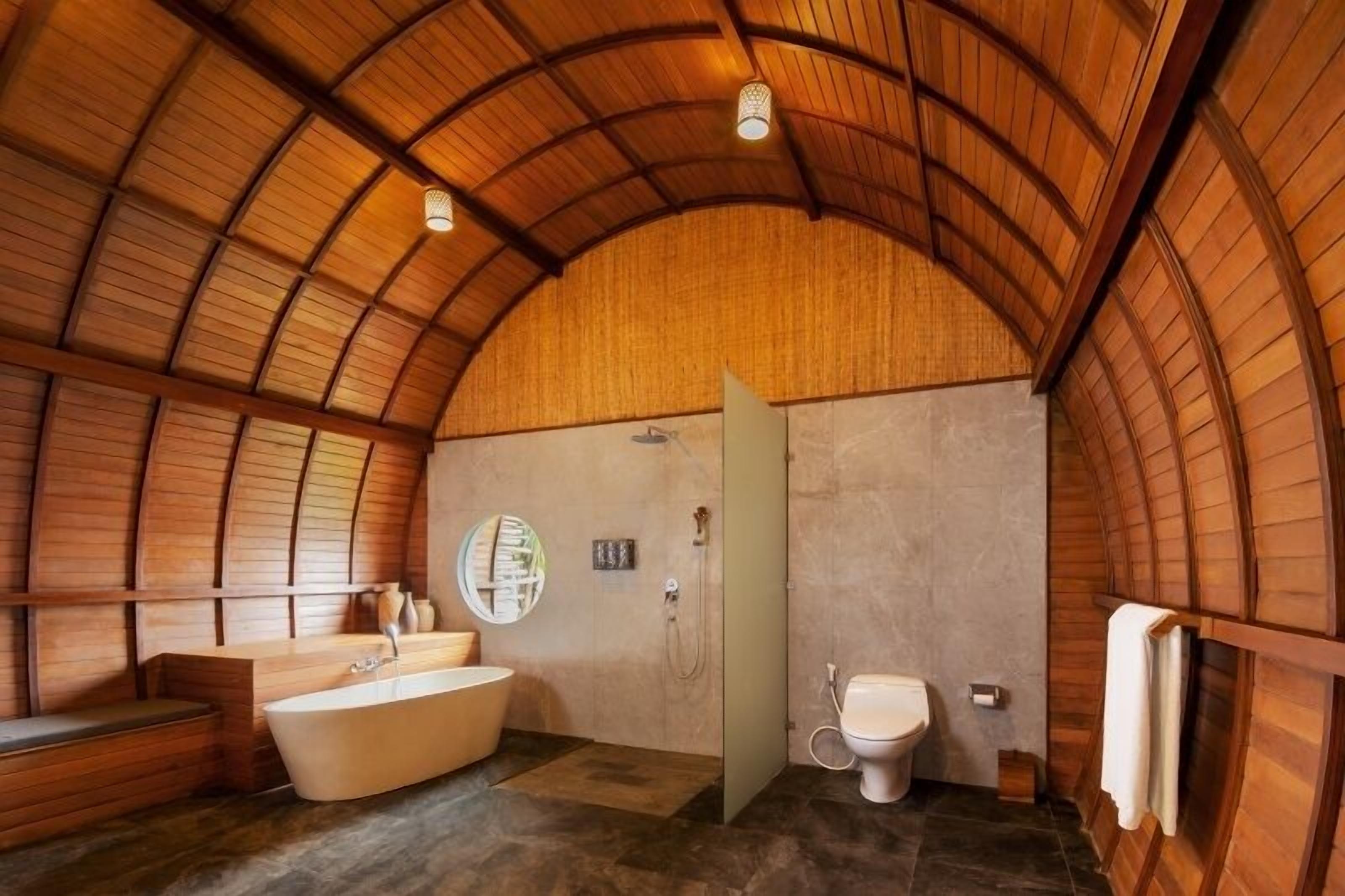 A bathroom with a bathtub, toilet, and sink, featuring a curved wooden ceiling and stone flooring.