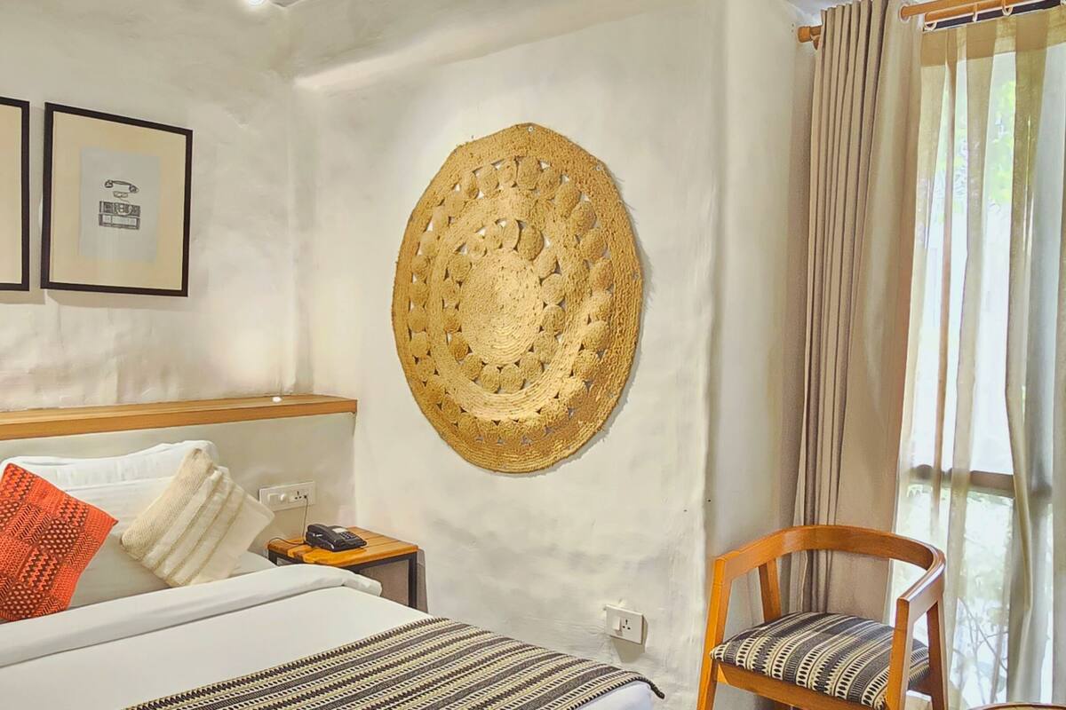 A hotel room with a bed, a chair, a wall-mounted decorative item, and curtains.