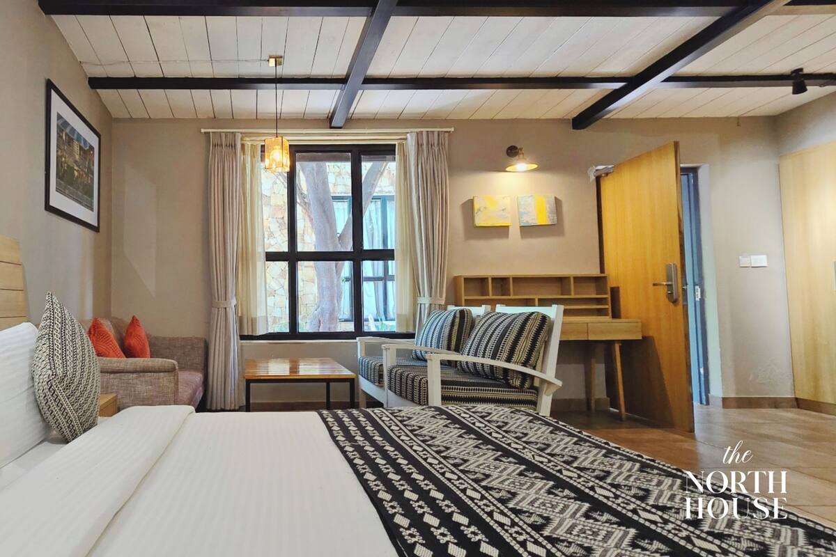 A hotel room with a bed, a sofa, a window with curtains, a small table, and a chair.