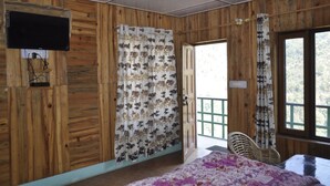 A wooden-paneled room with a bed, a television mounted on the wall, and a window with a view of greenery. - Hotel Garden Cottage & Resort Dhanaulti (Dhanaulti)