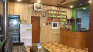 A room with a wooden interior, a Pepsi refrigerator, a television, a snack shelf, a bench, and a glass table. - Hotel Garden Cottage & Resort Dhanaulti (Dhanaulti)