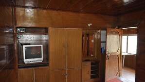 A wooden-paneled room with a television, a wardrobe, and a door leading to another room. - Hotel Garden Cottage & Resort Dhanaulti (Dhanaulti)